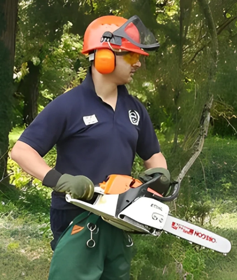 A search and rescue worker in a navy uniform holding a chainsaw with safety gear in a green environment.