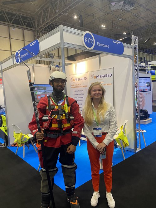Two individuals in front of an expo booth, one in rescue gear and the other in casual wear.