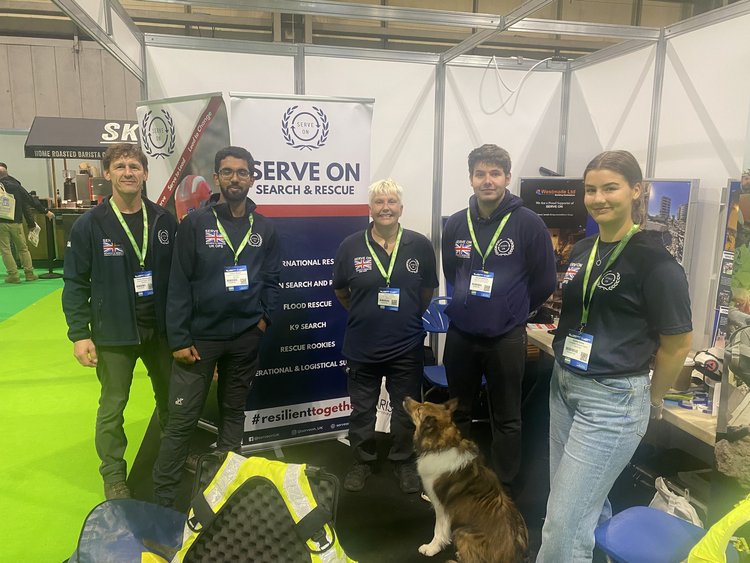 Five people, including a dog, posing at a booth at an expo.