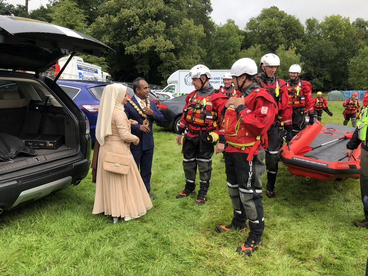 A group in safety gear discussing with a woman in a hijab and a man wearing a ceremonial chain.