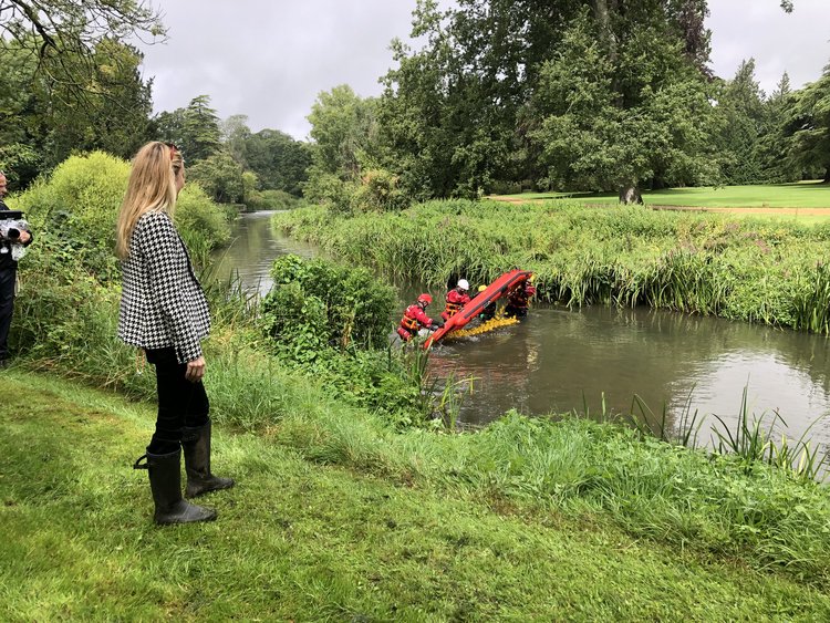 A woman watching a team in a small boat performing a drill in a park-like setting.