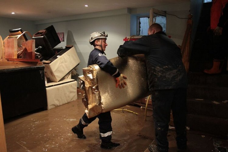 Two men carrying a metallic insulation sheet in a flooded basement.