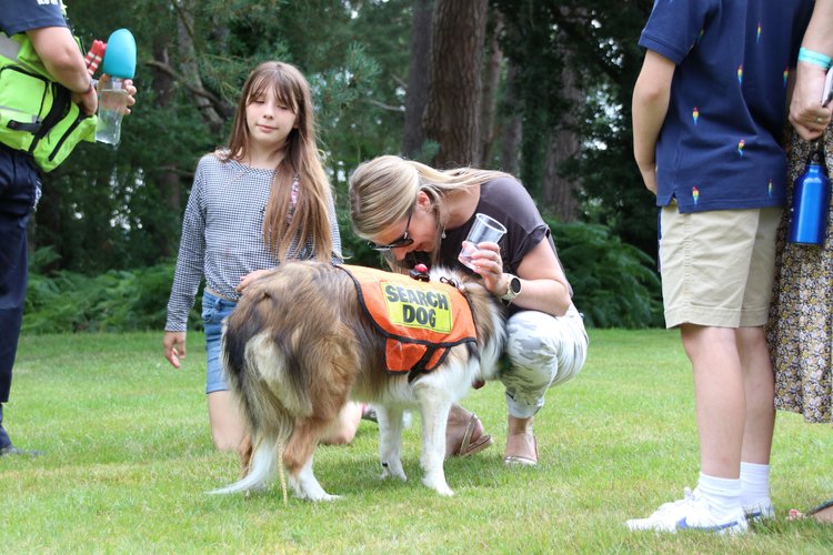 A woman interacting with a search dog in a park, with observers around.