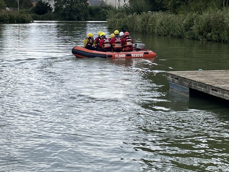 Rescue boat labeled "Flood Rescue" with team members aboard moving away from a dock on a river.