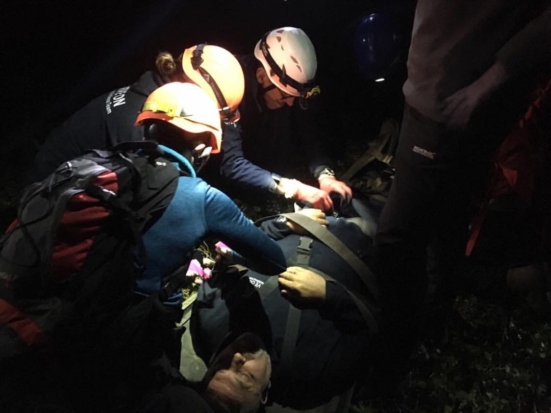 Nighttime rescue operation with workers gathered around a casualty, illuminated by headlamps.