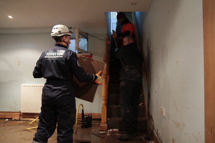 Three men, one observing, working on installing insulation in a house interior.