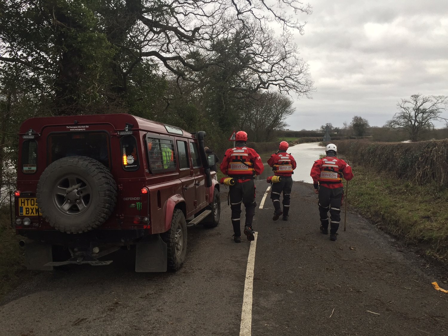 Emergency responders from Serve On walking towards a flooded area next to their vehicle.