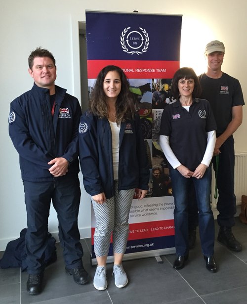 Four people in uniforms standing in front of a banner at an indoor event.