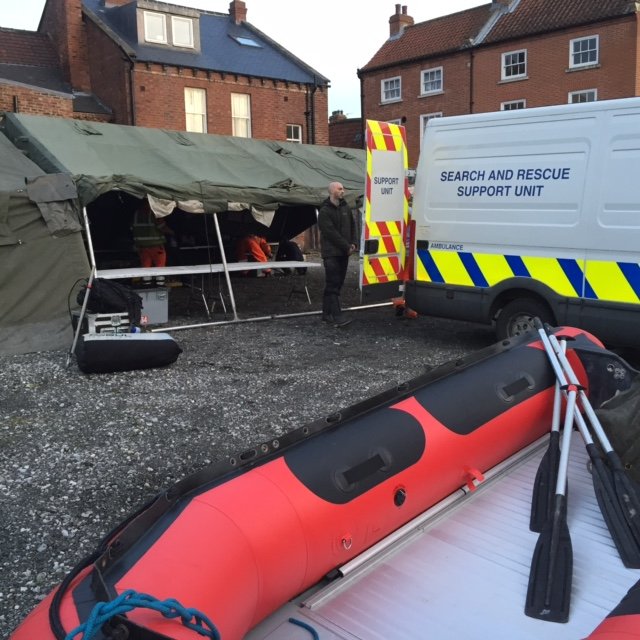 Search and rescue operation setup with a tent, a support vehicle, and equipment visible.