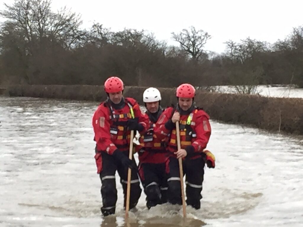 Three people wading through a flooded area in full rescue gear.
