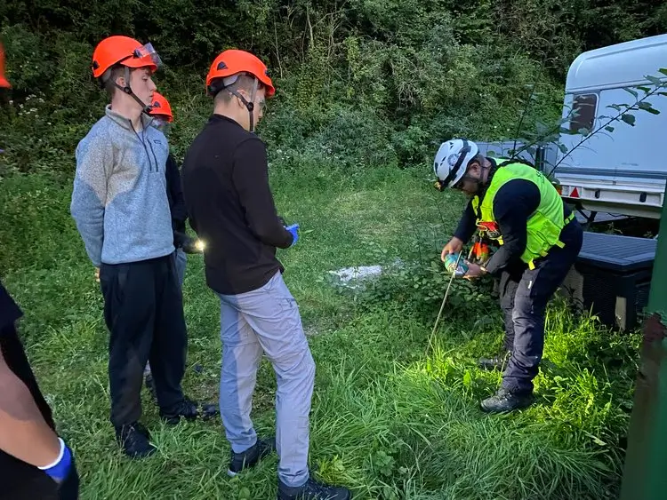 Rescue training in a field showing three men, two watching and one demonstrating equipment use.