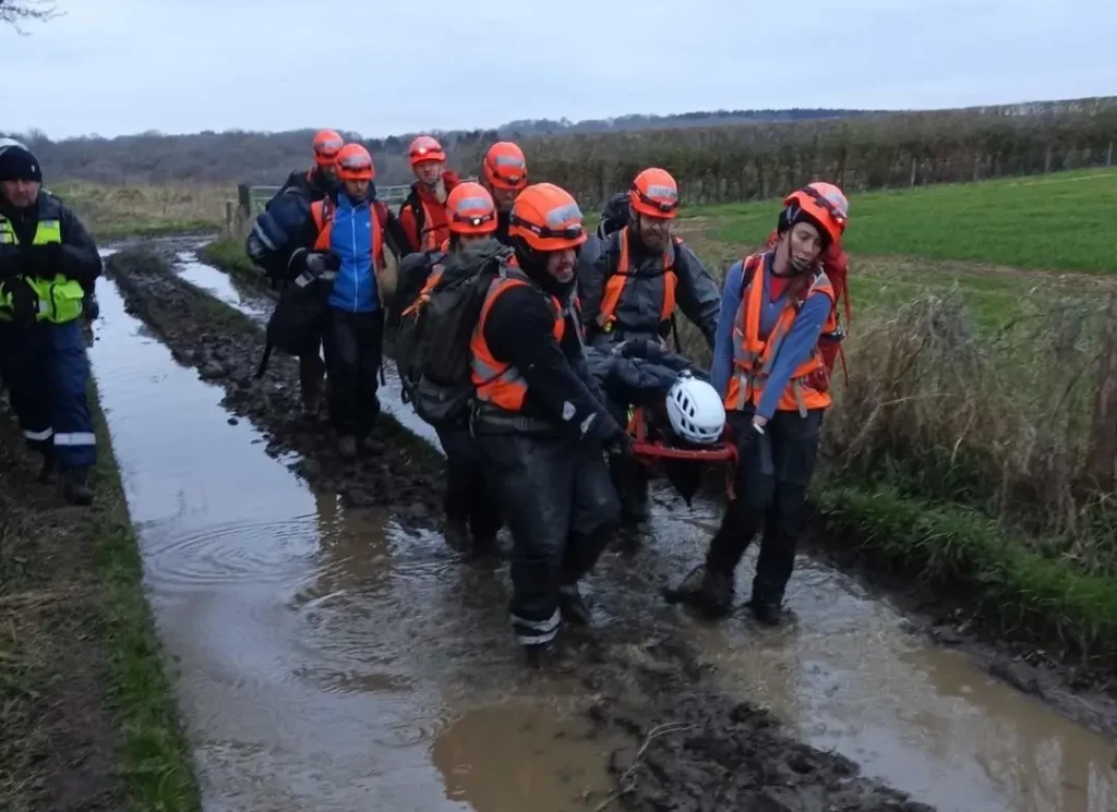 Rescue team carrying an injured person through a muddy field during a training exercise.