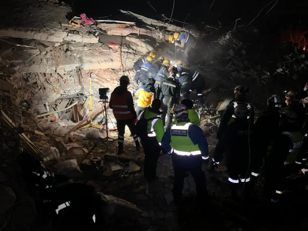 Search and rescue team working at night among debris with lighting equipment.