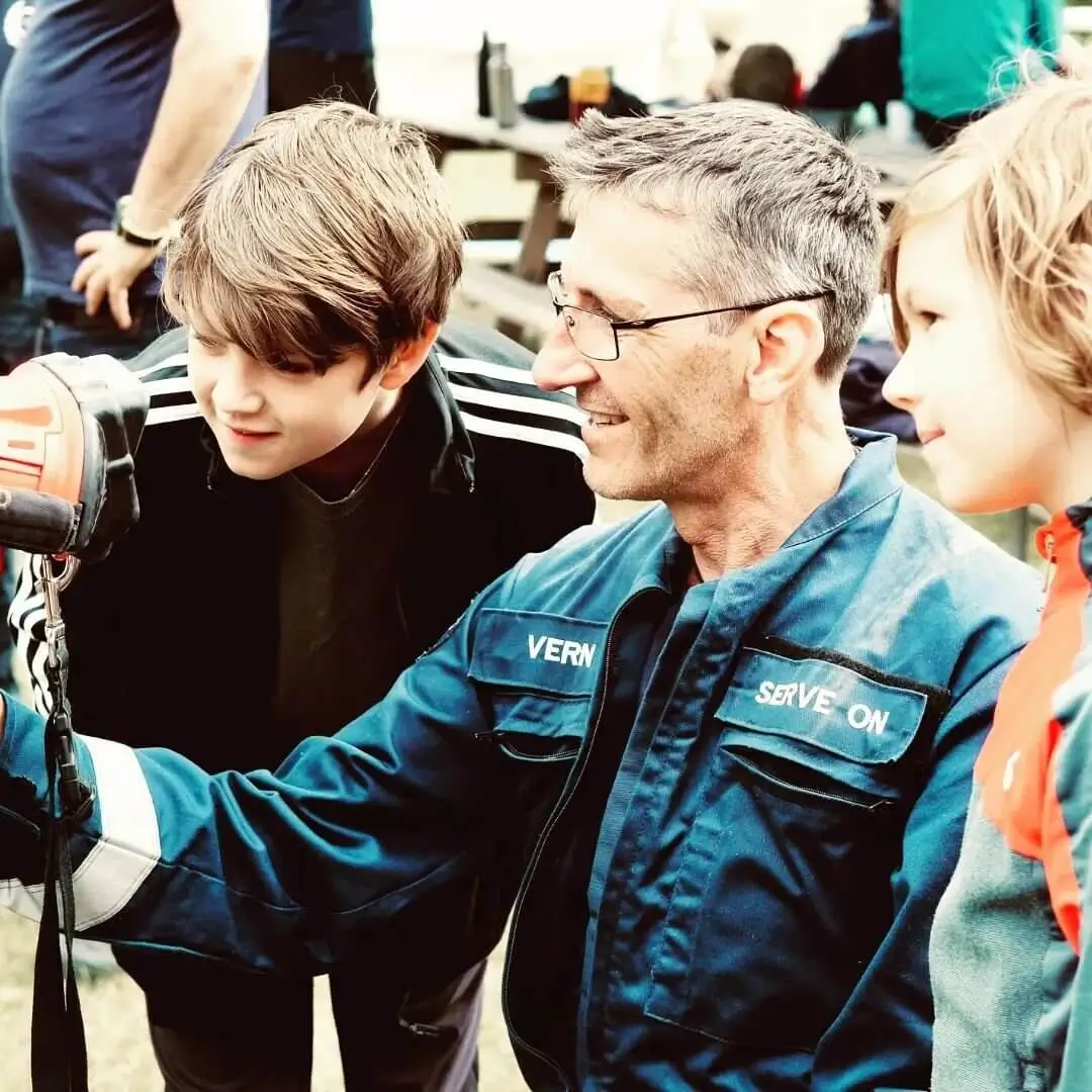 A man instructing two children on how to use a power drill during a community service event.