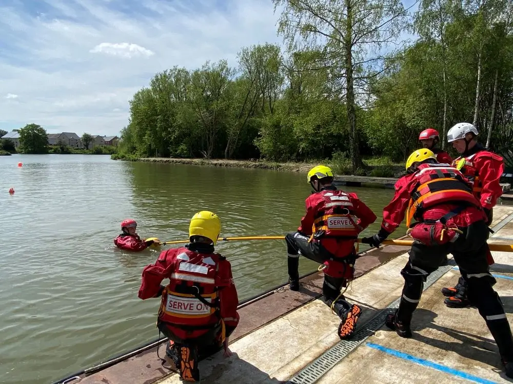 Search and rescue team practicing water rescue with ropes and flotation devices on a calm river.